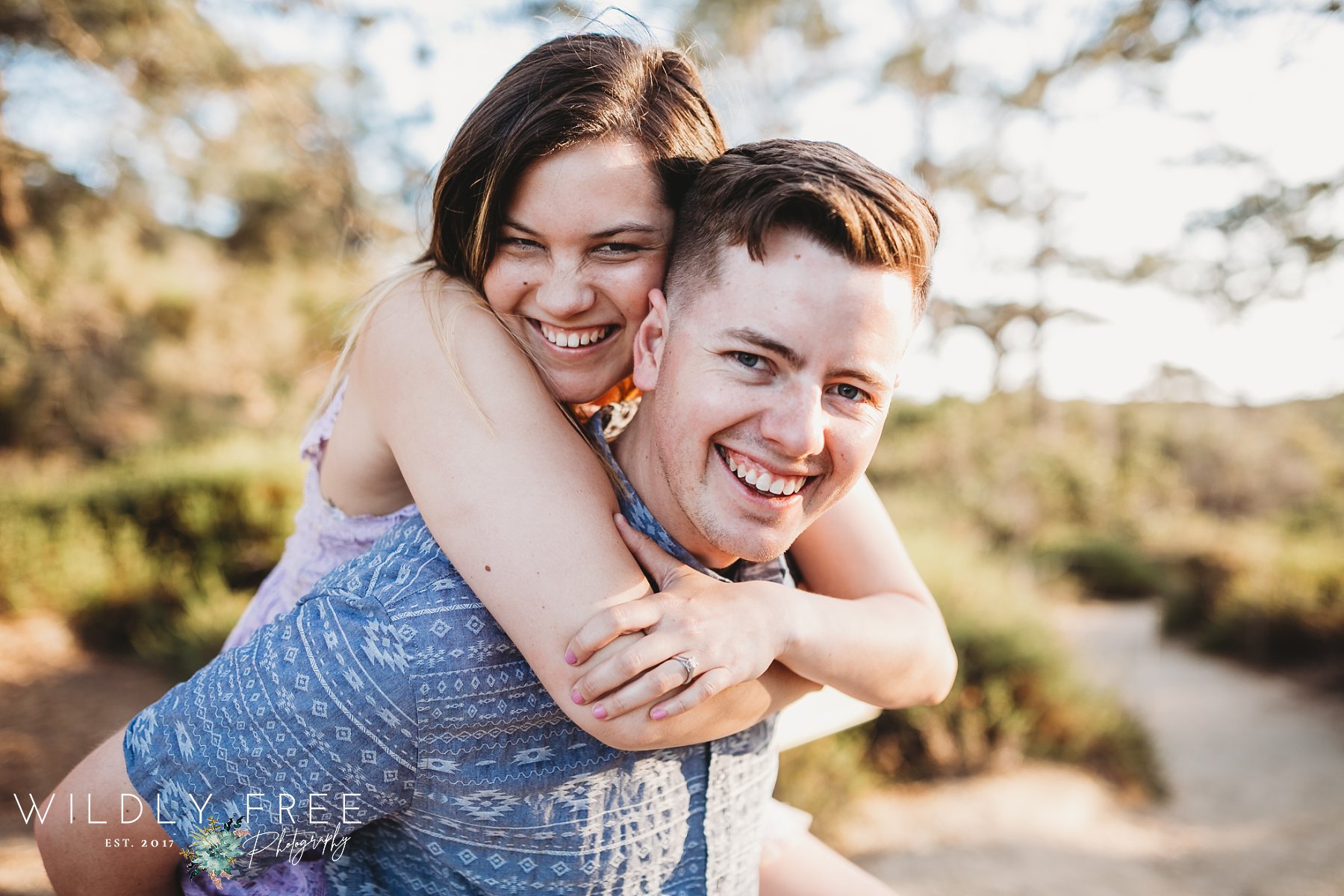 Engaged couple laughing into camera during piggy back ride