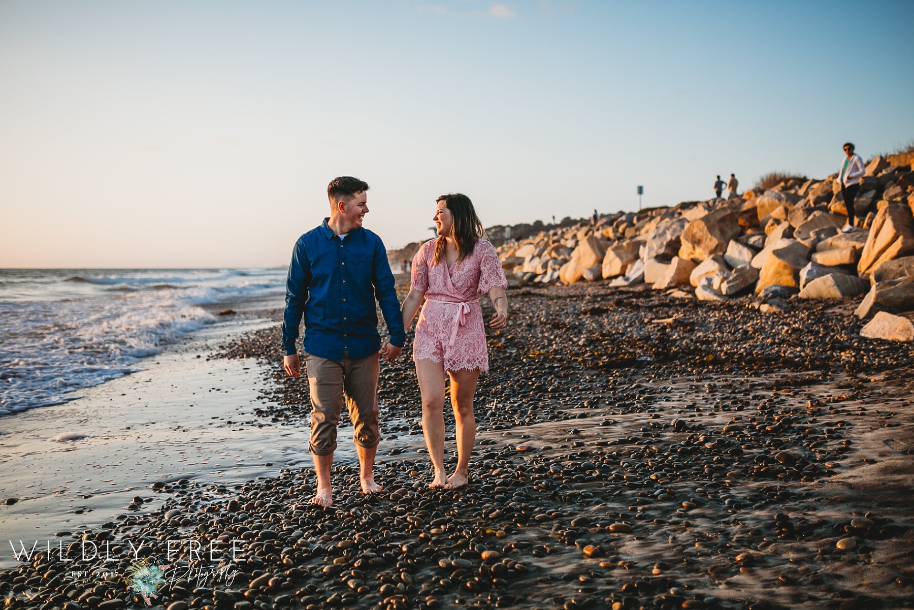 Engaged couple walking on rocky beach at Torrey Pines CA